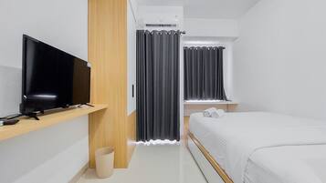 A modern hotel room with a flat-screen TV on a wooden shelf, a bed with white bedding, and a small bedside table.