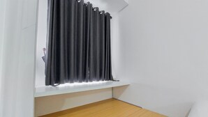 Una habitación con ventana, paredes blancas y suelo de madera.