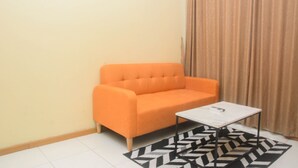 A small room with a single orange sofa and a white coffee table. - Elegant And Nice 2Br At Grand Palace Kemayoran Apartment (Jakarta)