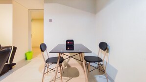A small, modern room with a table and two chairs, a trash bin, and a door leading to another room. - New And Nice 2Br At Marquis De Lafayette Apartment (Semarang)