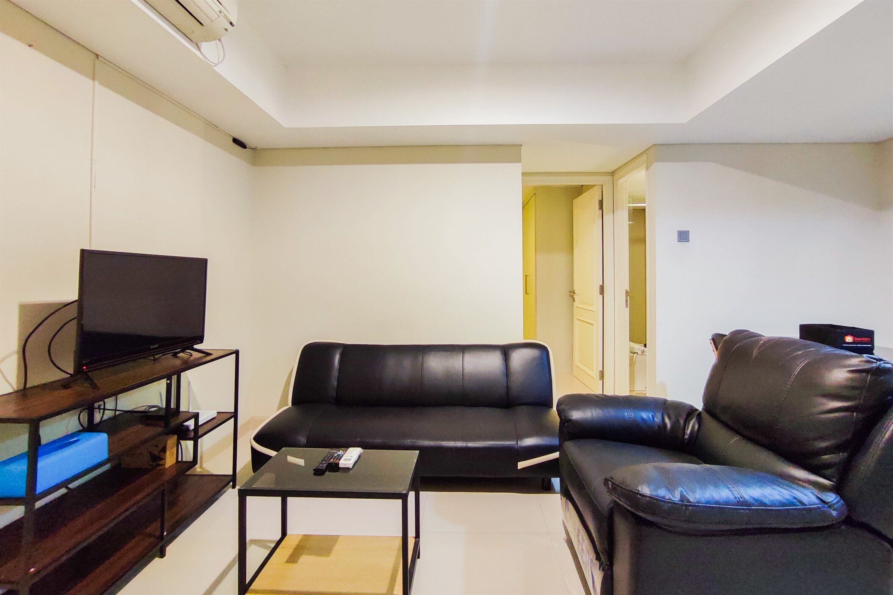 A living room with a black leather sofa, a television on a wooden stand, and a small table with a remote control.