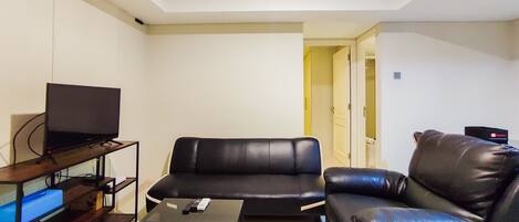 A living room with a black leather sofa, a television on a wooden stand, and a small table with a remote control.