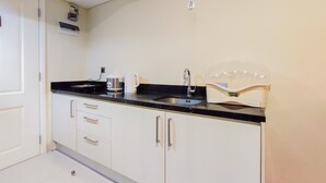 A small kitchenette with a black countertop, white cabinets, a sink, and a coffee maker. - New And Nice 2Br At Marquis De Lafayette Apartment (Semarang)