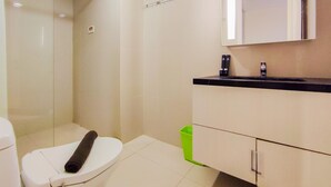 A bathroom with a toilet, a green trash bin, a sink, and a mirror above the counter. - New And Nice 2Br At Marquis De Lafayette Apartment (Semarang)