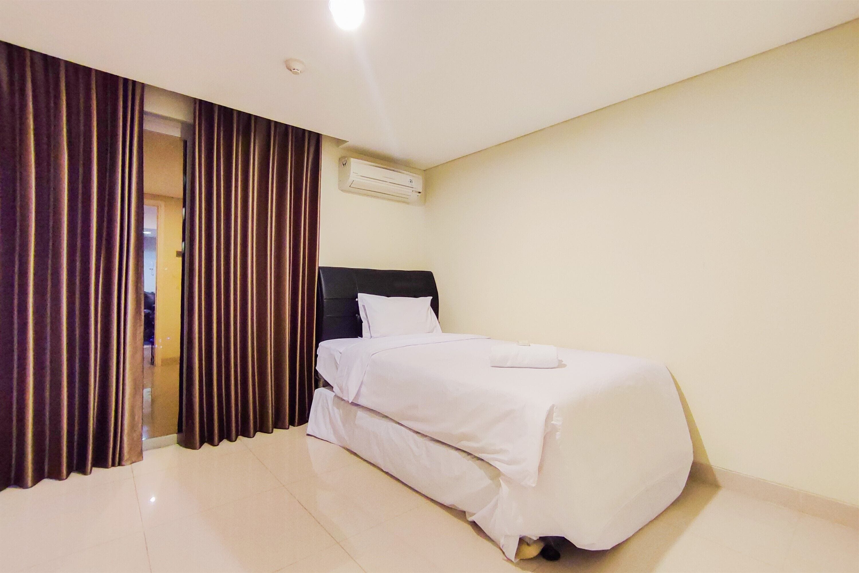 Ein Hotelzimmer mit Bett, Vorhängen, einer Klimaanlage und einem Fliesenboden.
