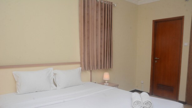 Une chambre d’hôtel avec un lit, des oreillers, une table de chevet avec une lampe et une porte.