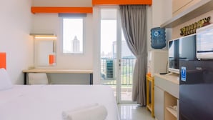 A hotel room with a bed, a desk, a television, a refrigerator, and a view of the city through the window. - Cozy Studio At 8Th Floor Signature Park Grande Apartment (Jakarta)