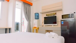 A hotel room with a bed, a TV, a microwave, a refrigerator, a water dispenser, and a window with curtains. - Cozy Studio At 8Th Floor Signature Park Grande Apartment (Jakarta)