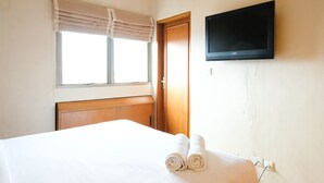 A hotel room with a bed, a TV mounted on the wall, a window with curtains, and a door. - Extra Spacious And Homey 2Br At Kondominium Puncak Marina Apartment (Surabaya)