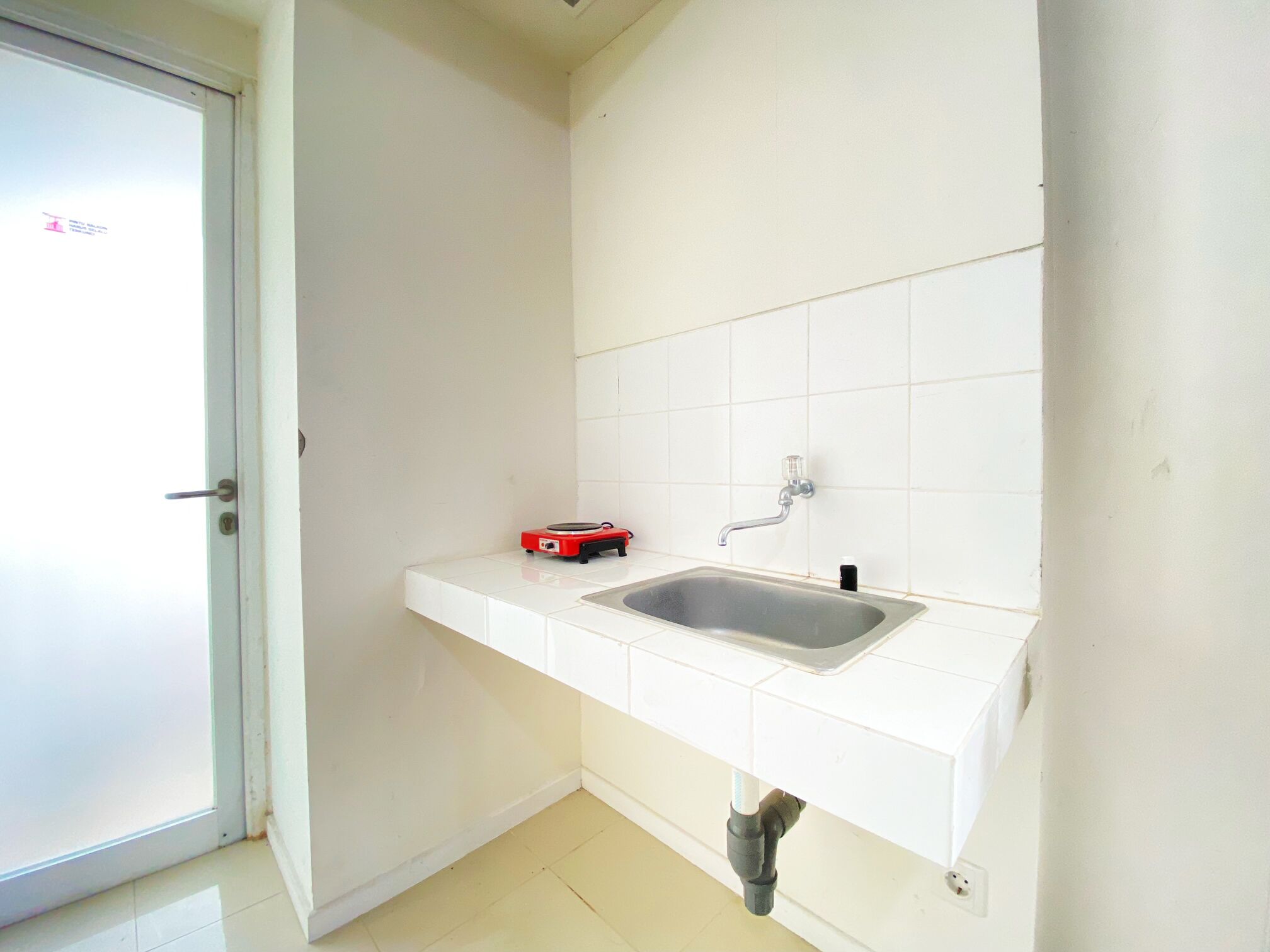 Ein kleines, sauberes Badezimmer mit einem weißen Waschbecken, einem Spiegel und einem roten Gegenstand auf der Ablagefläche.