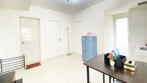 Una habitación amplia con un ventanal grande, una mesa de madera con sillas, un refrigerador azul y una puerta con perchero.
