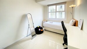 Una habitación pequeña y luminosa con cama, escritorio, silla, espejo de pie y ventana.
