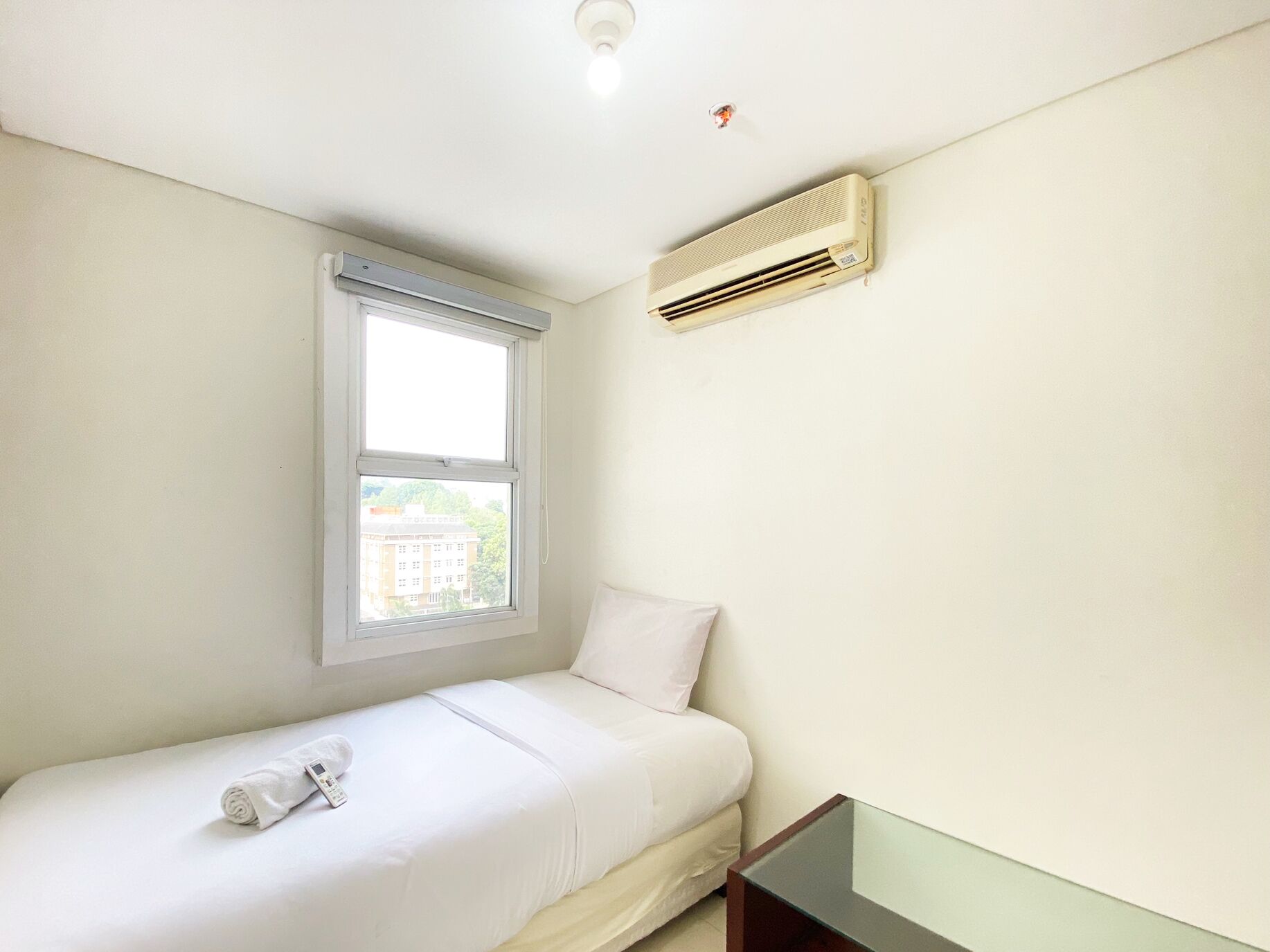 A small, clean room with a single bed, a window, and an air conditioning unit.