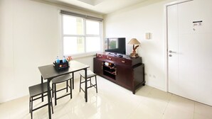 Una habitación pequeña y luminosa con televisión, un mueble de madera, una mesa con sillas y una ventana.
