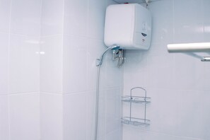 A bathroom with white tiles, a white water heater, a shower with a glass shelf, and a towel rack. - Simply And Well Design Studio Room At Patraland Urbano Apartment (Bekasi)