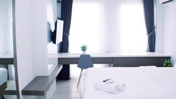 Et moderne hotelværelse med seng, skrivebord, stol og et vindue med gardiner.