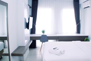 A modern hotel room with a bed, a desk, a chair, and a window with curtains. - Simply And Well Design Studio Room At Patraland Urbano Apartment (Bekasi)