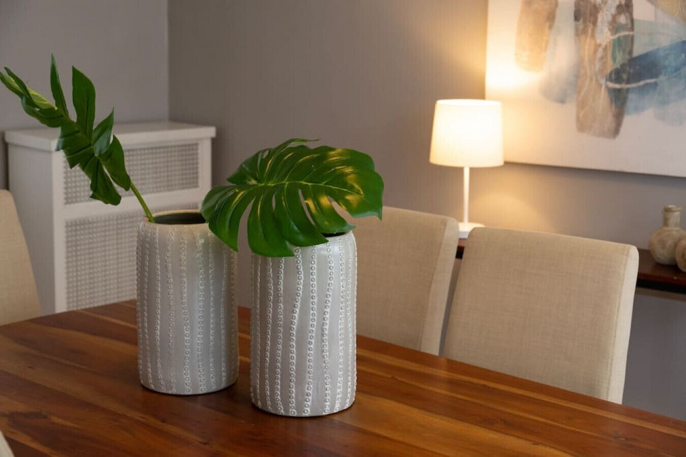 Two textured vases with green leaves on a wooden table.