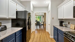 A modern kitchen with white cabinetry, a black refrigerator, and a wooden floor.