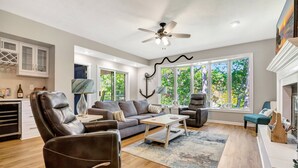 A modern living room with leather recliners, a sofa, a coffee table, and large windows offering a view of greenery.