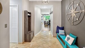 A hallway with a wooden bench, a wall clock, and a view into a dining area.