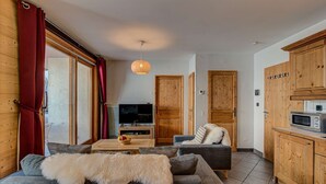 Ein gemütliches Wohnzimmer mit grauem Sofa, weichem Fellüberwurf, Holzschränken und einem Fernseher.
