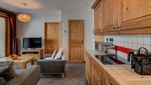 Ein kompakter Wohnbereich mit einer Küchenzeile, einer Couch, einem Fernseher und Holzschränken.