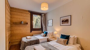 Ein gemütliches Zimmer mit zwei Betten, Holzwänden, einem Fenster mit Vorhängen, einem Regal mit Büchern und gerahmten Bildern an der Wand.