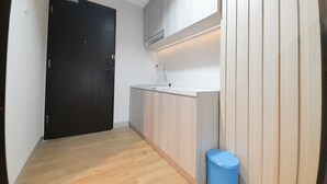 A modern kitchen with a black door, wooden cabinets, a white countertop, and a blue trash bin. - New Studio At Patraland Amarta Apartment (Ngaglik)