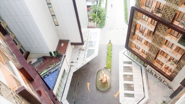 A courtyard with a central fountain, surrounded by modern buildings with balconies and a pool. - New Studio At Patraland Amarta Apartment (Ngaglik)