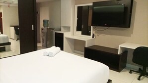 A hotel room with a bed, a desk, a chair, a television, and a minibar. - Luxurious Studio At Mataram City Apartment (Ngaglik)