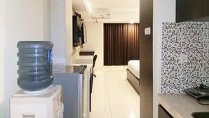 A hotel room with a kitchenette, a water dispenser, a bed, and a bathroom with a tiled wall. - Luxurious Studio At Mataram City Apartment (Ngaglik)