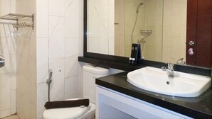 A bathroom with a white toilet, a sink with a black countertop, and a shower area. - Luxurious Studio At Mataram City Apartment (Ngaglik)