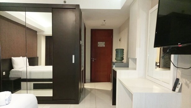 A hotel room with a bed, a desk, a television, and a wardrobe. - Luxurious Studio At Mataram City Apartment (Ngaglik)