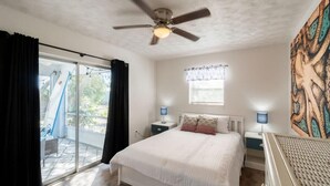 A bedroom with a bed, ceiling fan, nightstands, and a window with curtains.