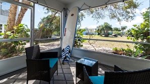 A covered outdoor seating area with wicker furniture and a surfboard leaning against the wall.