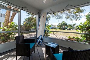 A covered outdoor seating area with wicker furniture and a surfboard leaning against the wall.