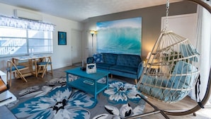 A living room with a sofa, a hanging chair, a coffee table, a rug, and a painting of a wave.