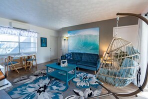 A living room with a sofa, a hanging chair, a coffee table, a rug, and a painting of a wave.