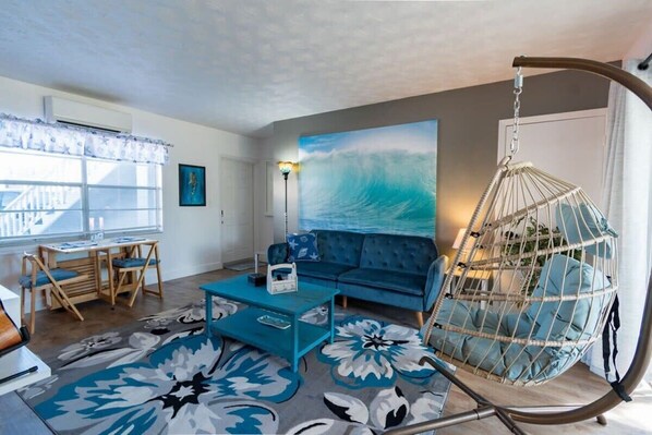 A living room with a sofa, a hanging chair, a coffee table, a rug, and a painting of a wave.
