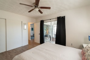 Une chambre Ă coucher comprenant un lit, un ventilateur de plafond, une porte-fenĂȘtre coulissante avec des rideaux et une vue sur un espace extĂ©rieur.