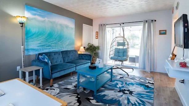 A living room with a blue sofa, a hanging chair, a coffee table, and a large painting of a wave.