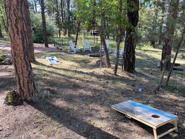 Un área boscosa con un juego de mesa de madera, sillas blancas y un columpio.