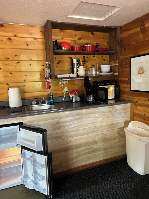 A compact kitchen with wooden walls, a built-in sink, a coffee maker, and a microwave.