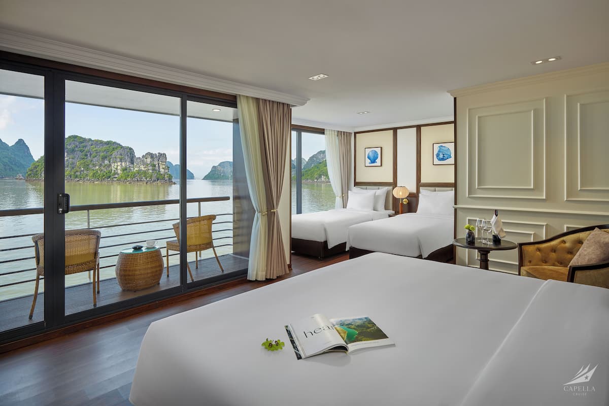 Hotelkamer met een groot bed, twee nachtkastjes, een bank en een balkon met uitzicht op een meer en bergen.