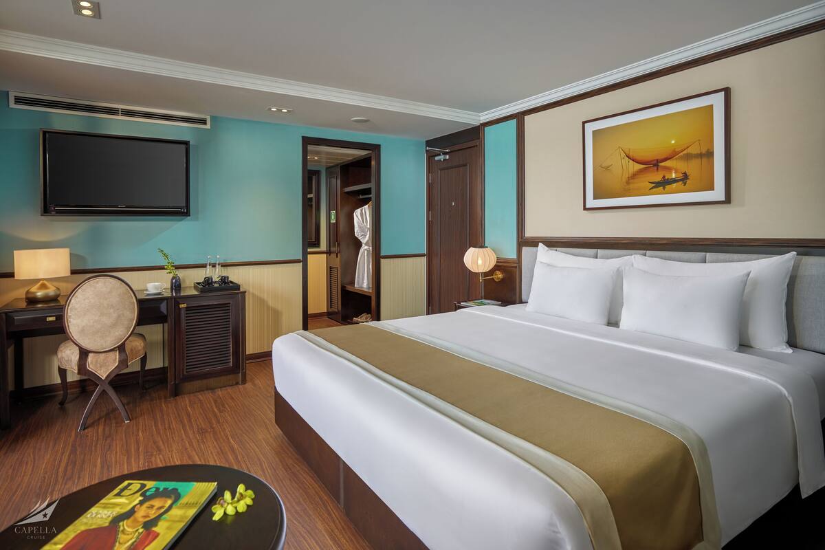 Een hotelkamer met een groot bed, een bureau met stoel, een flatscreen televisie en een schilderij aan de muur.