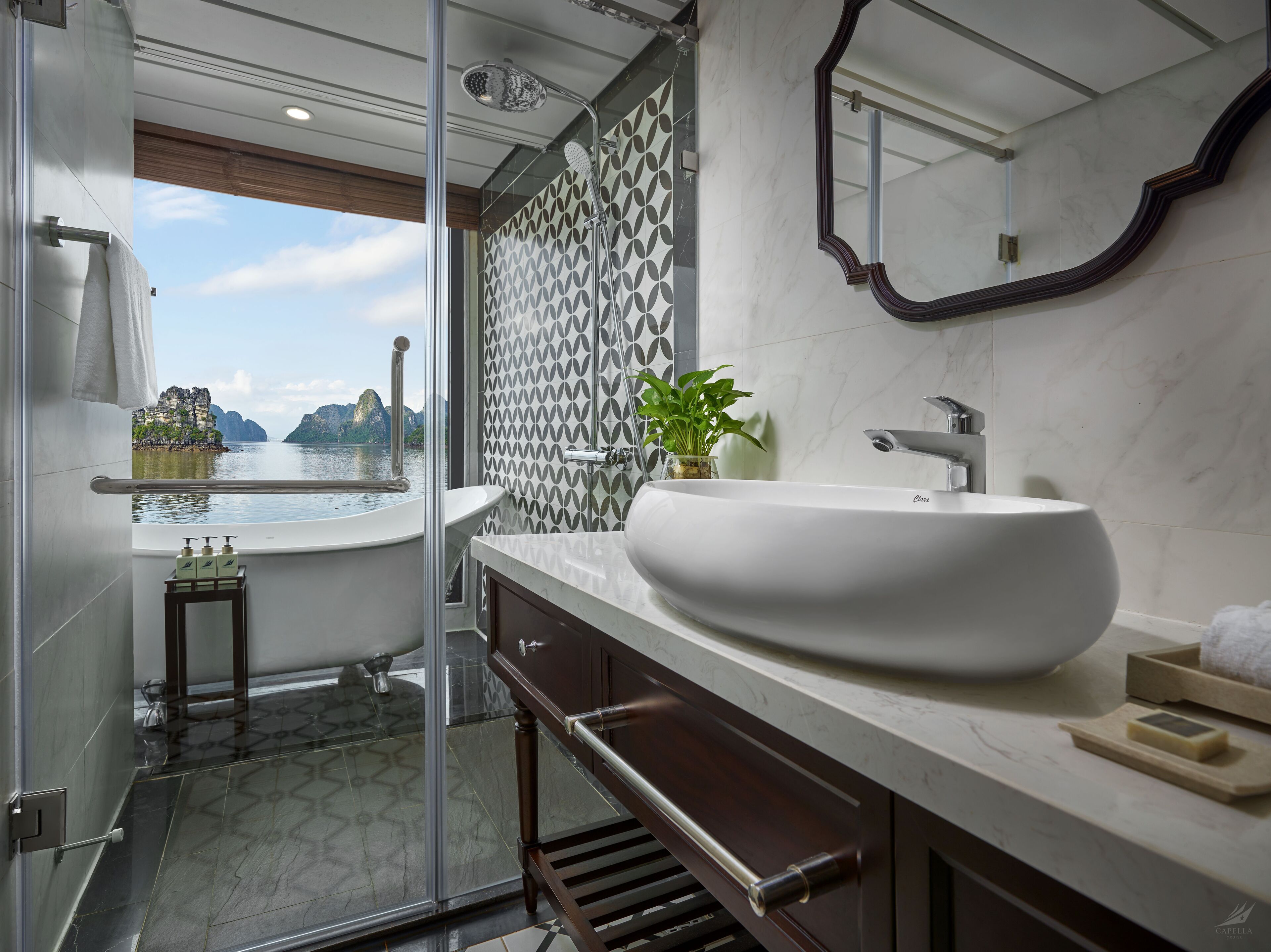A modern bathroom with a large bathtub, a white sink, and a shower. There is a view of a mountainous landscape through the window.