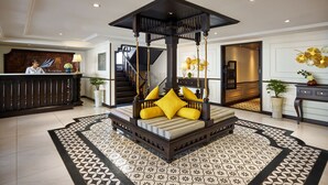 A lobby with a central bed with yellow pillows, a reception desk, and a staircase. - Halong CAPELLACRUISE - Member of Lyra Cruise Collection (Tuan Chau)