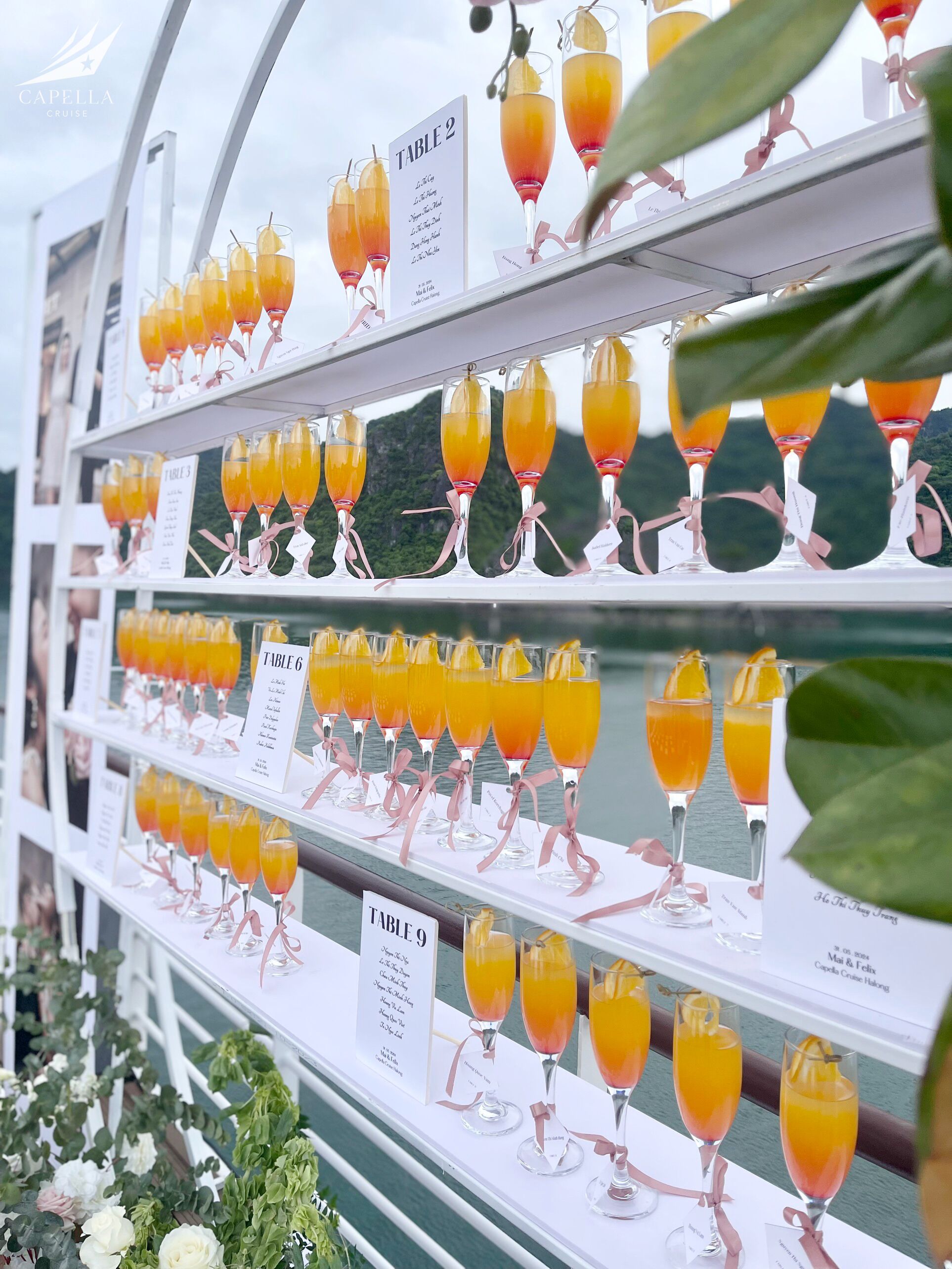 A table setting with multiple glasses of orange juice, each with a pink ribbon and a label indicating the table number.