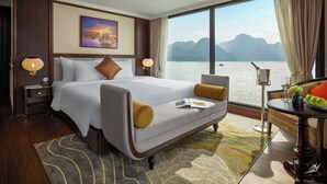 A hotel room with a large bed, a view of the water, and a table with a vase and apples. - Halong CAPELLACRUISE - Member of Lyra Cruise Collection (Tuan Chau)